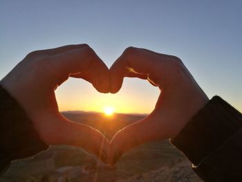 Close-up of hand holding heart shape against sunset sky