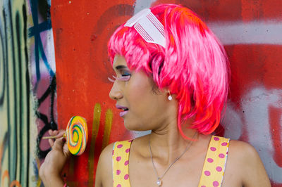 Woman with pink hair holding lollipop against graffiti wall