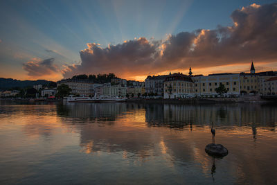 Buildings by river against sky during sunset