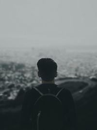 Rear view of man standing at beach against sky