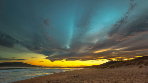 Scenic view of beach against dramatic sky during sunset