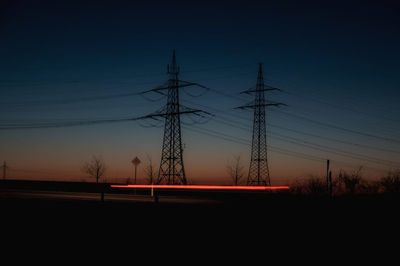 Silhouette electricity pylon on field against sky at sunset