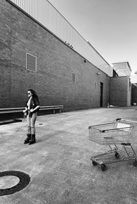 Full length of woman standing on footpath against wall