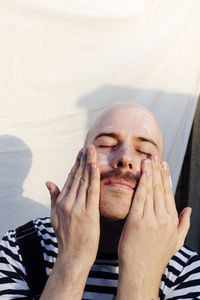 Man with eyes closed applying moisturizer in front of white backdrop