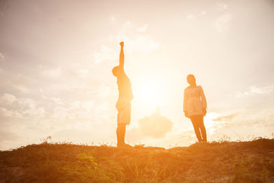 Rear view of friends standing on field against sky during sunset