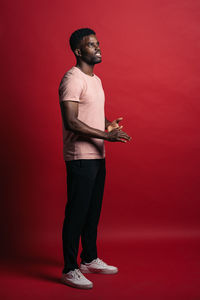 Side view of young man looking away against red background