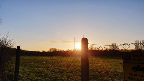 Fence on field against sky during sunset