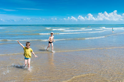 Siblings playing at beach against sky