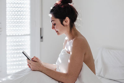 Side view of young woman using mobile phone on bed