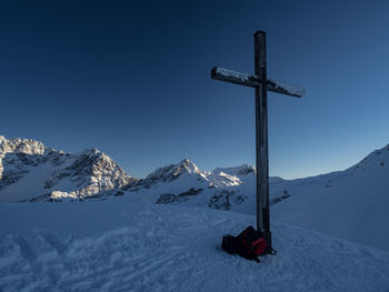 Scenic view of wooden cross by snowcapped mountains against clear blue sky