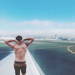Rear view of shirtless man standing in city against sky