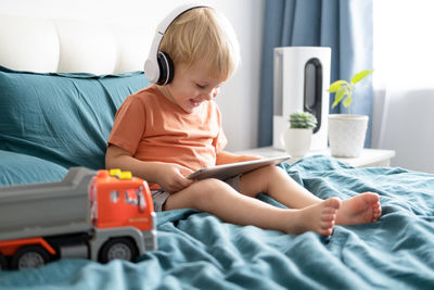 Smiling boy using digital tablet sitting on bed at home