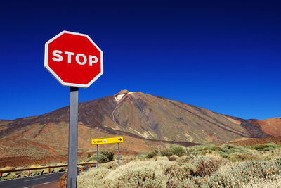 Stop sign by rocky mountain at el teide national park against clear blue sky