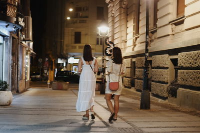 Rear view of women walking on street amidst buildings