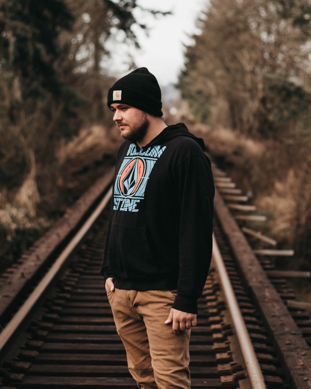 railroad track, rail transportation, track, one person, real people, lifestyles, transportation, leisure activity, focus on foreground, young men, young adult, tree, standing, day, casual clothing, nature, plant, looking, outdoors