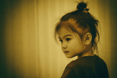 Close-up of cute girl standing against curtain