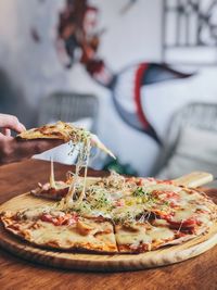 Cropped hand holding pizza at table