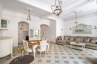 Classic room with dining table,  sofa, tile floor, light walls and vintage chandeliers.