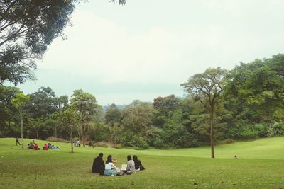 People relaxing on field against trees