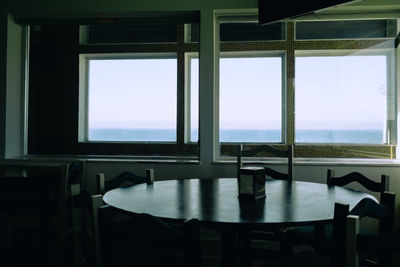 Empty chairs and table by sea against sky