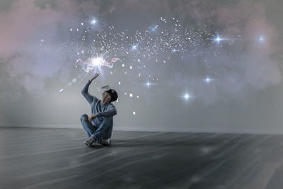 Young man in empty apartment sitting on the floor using virtual reality glasses, composite