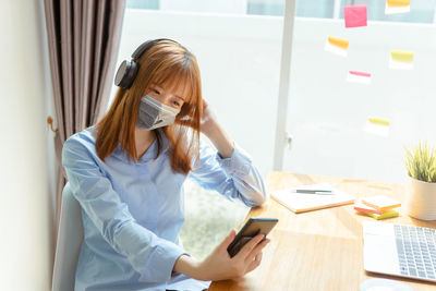 Young woman using phone while sitting on table