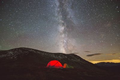 Illuminated tent on balkan mountains against constellations in sky