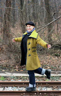 Smiling woman with arms outstretched standing on railroad track during winter