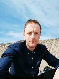 Portrait of man sitting at beach against sky on sunny day