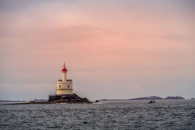 Lighthouse by sea against sky during sunset