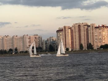 Sailboats in sea by buildings against sky