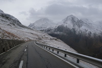 Road leading towards snowcapped mountains against sky