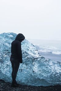 Man standing in sea against sky during winter