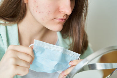 Unknown female teenager with acne taking off medical mask