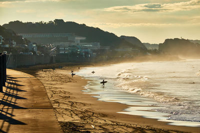 Scenic view of beach with silhouette people against moody sky during sunrise