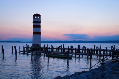 Lighthouse by sea against sky during sunset