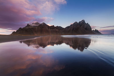 Scenic view of mountain reflected on wet beach during sunset
