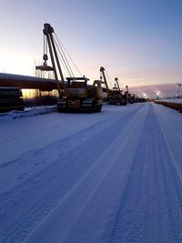 Cars on snow covered land against sky during sunset