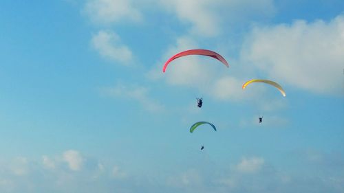 Low angle view of people paragliding against blue sky