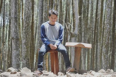 Portrait of smiling young man sitting against trees in forest