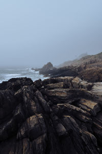 Scenic view of rocks at beach against sky during foggy weather