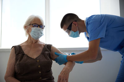 Doctor wearing mask vaccinating patient at hospital