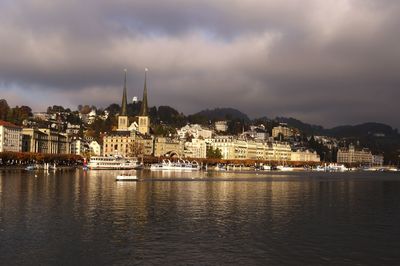 View of city at waterfront against cloudy sky