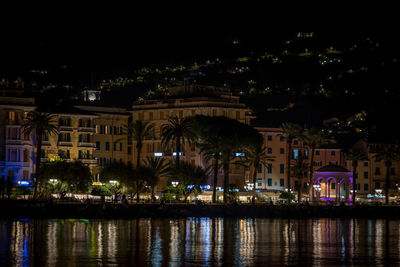 Illuminated buildings by river in city at night