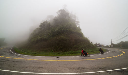 People riding motorcycle on road against trees