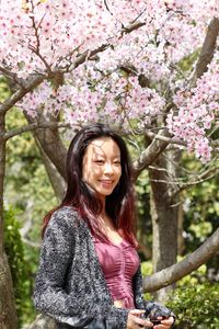 Smiling teenage girl standing against tree in park