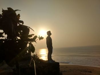 Silhouette man standing at beach against sky during sunset