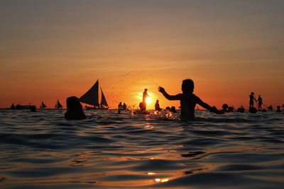 Silhouette people on sea against sky during sunset