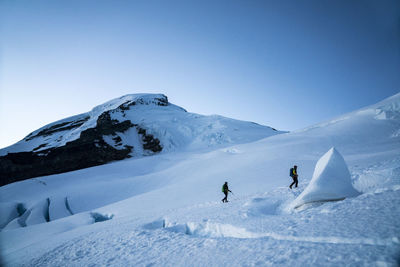 Two mountaineers hike up a glacier, the summit of mt. baker in the background