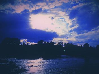 Silhouette trees by calm lake against cloudy sky